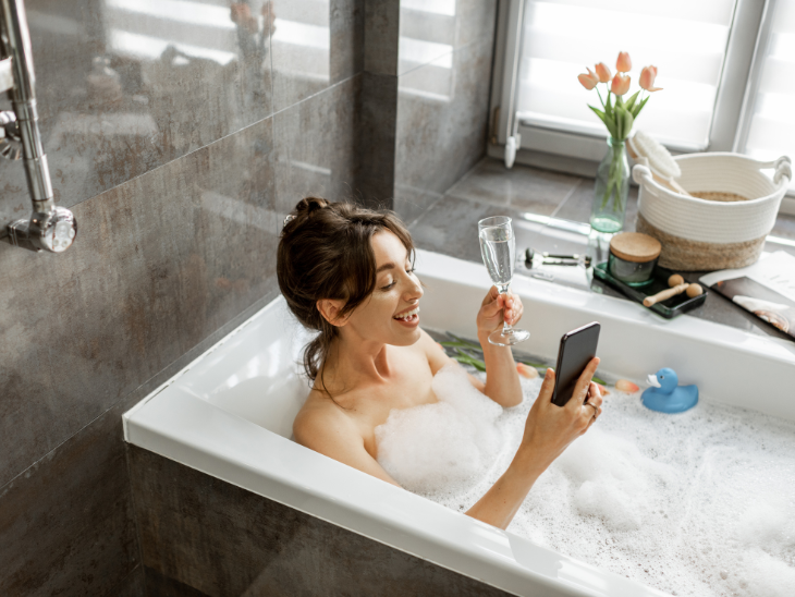 Woman lying in bath with a glass of wine and mobile phone.