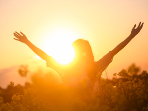 A woman facing a sunrise with her arms stretched into the air. She is feeling gratitude! Gratitude is a Powerful Tool that Improves Our Lives